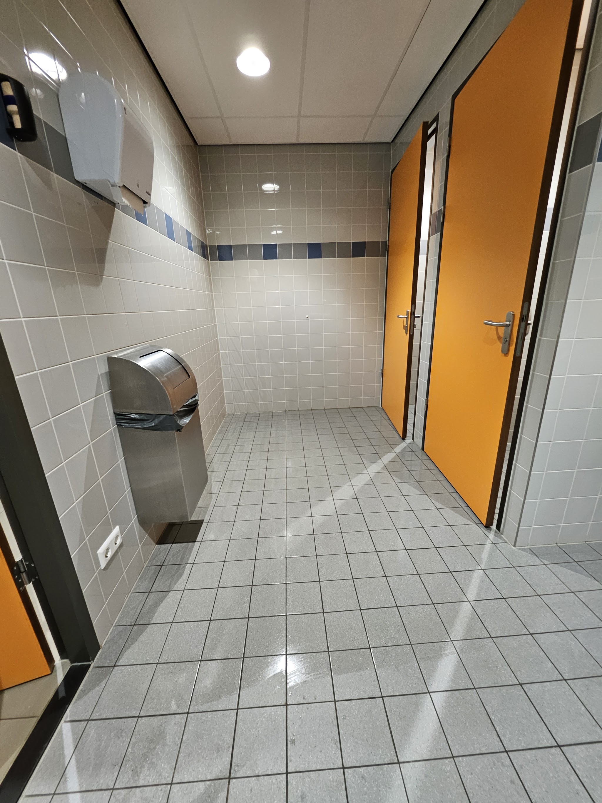 Betegelde sanitaire ruimte met oranje deuren en een schone vloer
